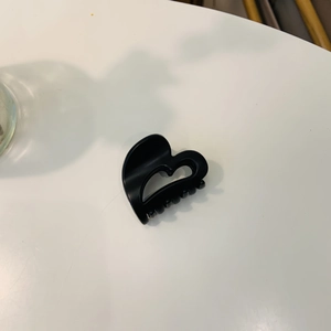 Close-up of a black heart-shaped acetate hair claw clip on a minimalist white surface