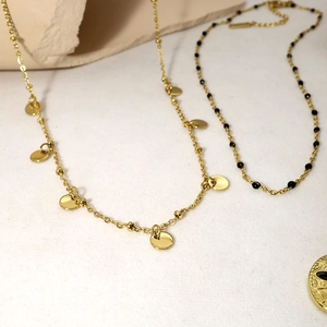 Detailed view of layered gold necklaces with black beads and circular sequin pendants