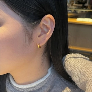 Close-up of a gold hexagonal hoop earring worn by a model in a minimalist style