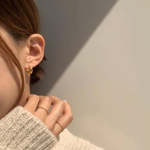 Macro detail of gold twisted hoop earrings worn by model with minimalist warm lighting