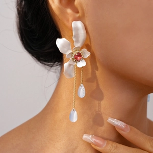 Detail of white flower drop earring with red crystal center and long golden tassels