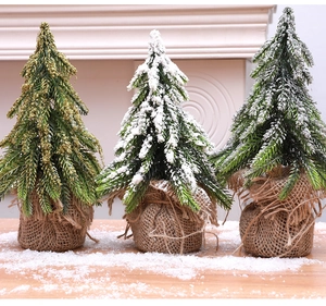 Three mini flocked Christmas trees with burlap bases and gold ornaments on a snowy wood surface