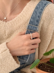 Detail shot of a silver twisted rope ring and heart pendant necklace on a model