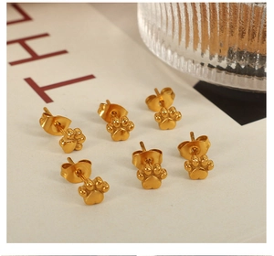 Détail de six boucles d'oreilles pattes de chat dorées mates sur fond beige
