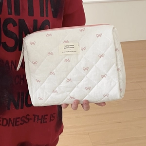 Détail de la trousse à maquillage blanche matelassée avec nœuds roses et fermeture éclair