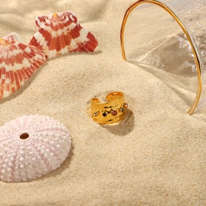 Detail eines breiten, gehämmerten Goldrings mit farbigen Zirkonia auf Strandsand