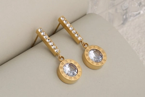 Detail of gold drop earrings with Roman numeral engraving and cubic zirconia crystal