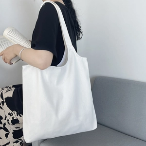 Side view of a white canvas tote bag worn by a model in a minimalist home setting