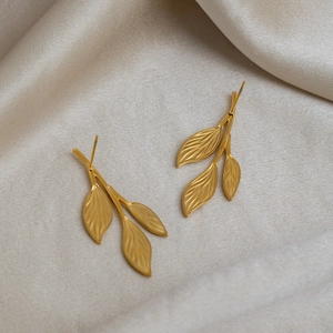 Minimalist leaf stud earrings in 18K gold plated stainless steel on beige fabric