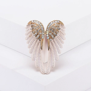 Elegant gold angel wing brooch with white enamel and sparkling rhinestones on a white stand