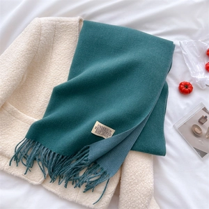 Close-up of dark green cashmere-feel scarf with fringe and label on a beige fleece jacket