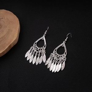 Detailed close-up of hollow teardrop earrings with leaf fringe tassels on black leather