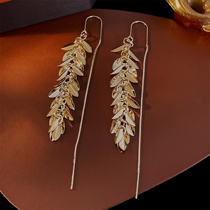 Detail of long gold leaf tassel drop earrings on luxury brown textured leather background