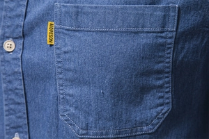 Close-up of blue denim shirt pocket with beige button and fine stitching detail