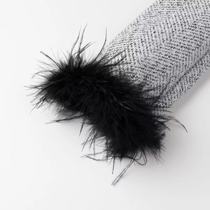 Detail of grey herringbone fabric sleeve featuring elegant black feather trim at the cuff