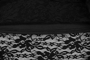 Macro detail of intricate black floral lace fabric with fine mesh texture and hem seam work