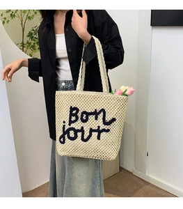 Detailed view of beige straw tote bag with black Bon jour embroidery and woven texture