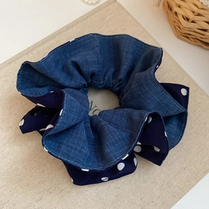 Close-up of blue denim and white polka dot fabric scrunchie on a textured book surface