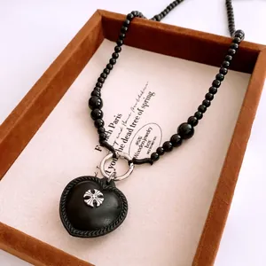 Beaded necklace featuring a black leather heart pendant with a silver cross insignia
