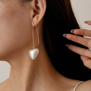 Detail of vintage heart pearl drop earrings worn by a model with elegant gold finish