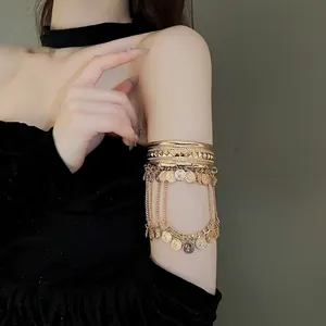 Gold upper arm cuff with chain tassels and coin pendants on model against grey background