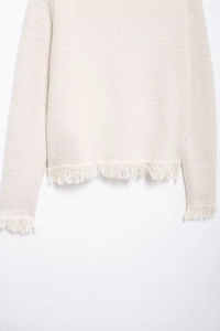Close-up of beige knit cardigan fabric texture with elegant fringe detail hem