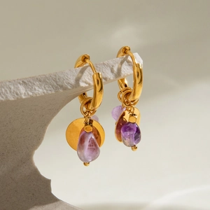 Détail de boucles d'oreilles martelées dorées avec pierre naturelle violette sur support roche