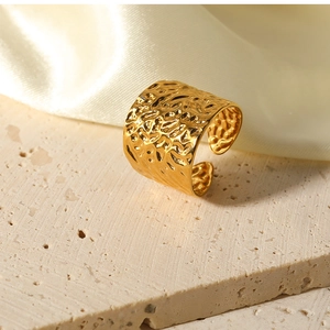 Detail of wide gold hammered ring with lava texture on beige stone and silk surface