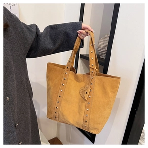 Detail view of ginger yellow suede tote bag featuring metallic rivet accents and heart charm