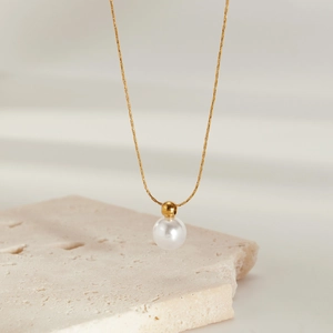 Elegant gold titanium steel necklace featuring a round white pearl on a textured stone slab
