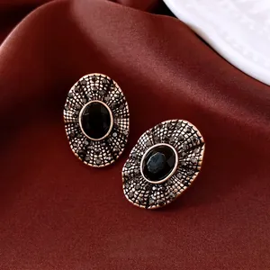 Vintage oval black gemstone stud earrings with gold filigree on red silk background