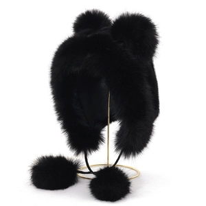 Close-up of black faux fur earflap hat with fluffy pom-poms on a gold metal stand