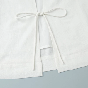 Detailed close-up of white woven fabric with elegant tie-up bow closure and clean stitching
