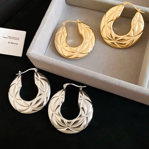 Detailed close-up of chunky gold and silver hoop earrings with quilted geometric textures