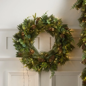 Lush PE Christmas wreath with pine cones and warm LED lights on a white wall