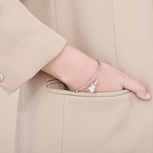 Close-up of silver guitar pendant bracelet worn by model with beige suit background