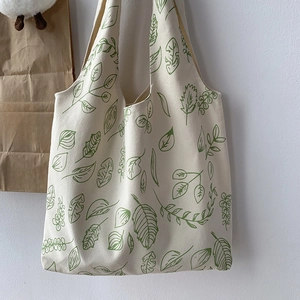 Detailed view of beige canvas tote bag with fresh green leaf prints and textured fabric