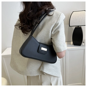 Detail of minimalist black baguette bag with gold buckle on shoulder in modern interior
