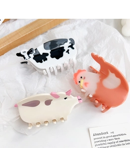 Macro shot of pig, cow, and rooster acetate hair claws on a textured white background