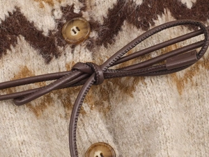 Dettaglio ravvicinato della maglia jacquard beige con cordino in pelle e bottone