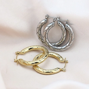 Macro detail of chunky twisted hoop earrings in gold and silver finish on silk fabric