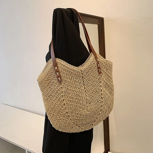 Close-up of hand-woven hollow straw tote bag with brown leather straps and white stitching