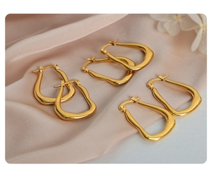 Three pairs of geometric gold titanium steel earrings on soft pink silk fabric background