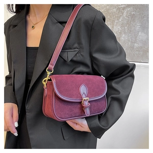 Detail of burgundy suede shoulder bag with vintage gold buckle on black blazer