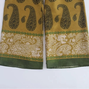 Gros plan sur les motifs paisley et les coutures du pantalon en satin jaune moutarde