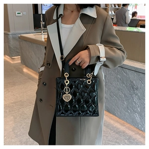 Detail of black patent leather quilted bag with gold heart charm on a trench coat