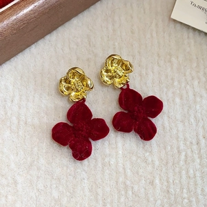 Detailed close-up of velvet wine red floral earrings with golden petals on soft plush surface