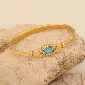 Gold Claddagh bracelet with blue heart gemstone on a natural stone background