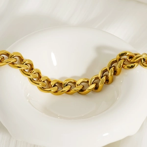 Polished 18k gold plated chunky Cuban link bracelet on a white ceramic plate