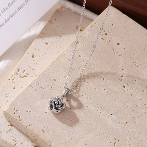 Elegant silver rose flower pendant necklace draped over a textured stone aesthetic display